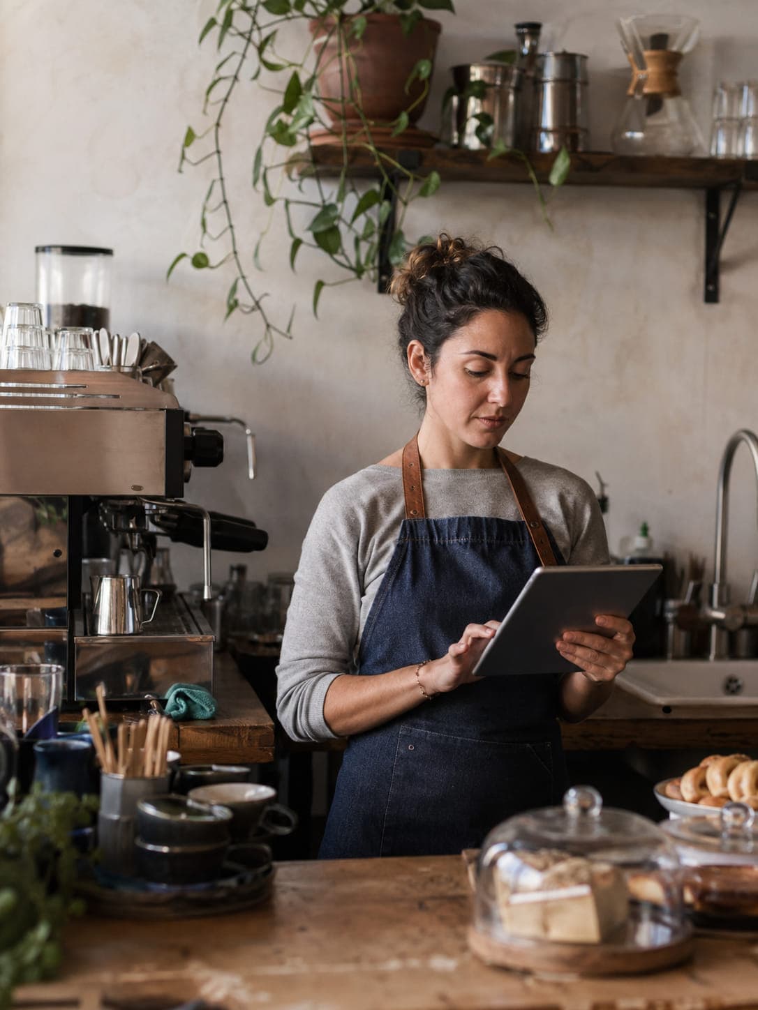 An independent café owner checking her tablet beside the coffee counter.